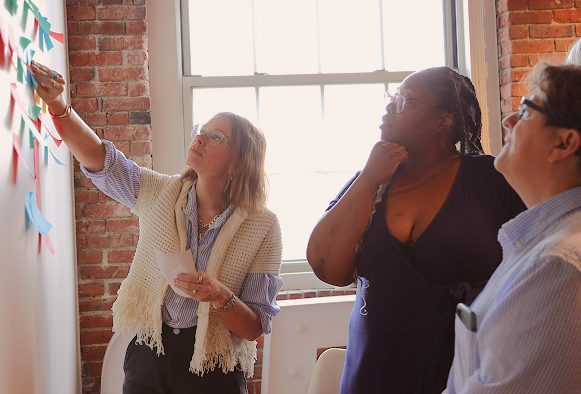 Two people stand by a window and place sticky notes on a wall during a collaborative activity.