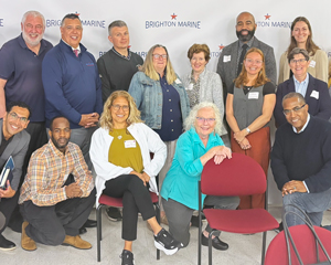 A group of people pose together in front of a Brighton Marine backdrop at an indoor event.