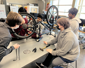 Students collaborate in a workshop classroom to repair and reassemble a bicycle.